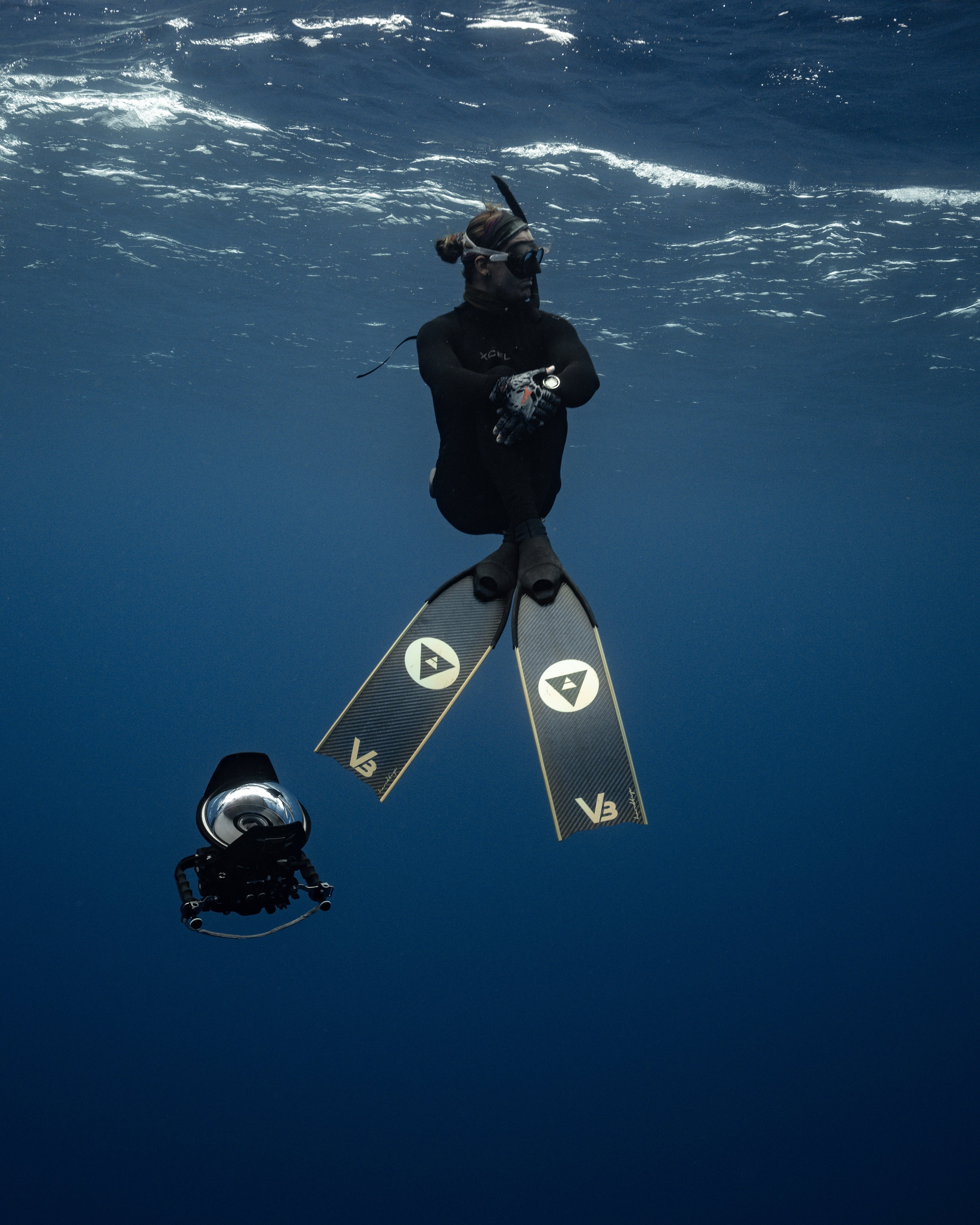 An underwater photographer floating in water with his DSLR camera with housing, wearing a pair of Alchemy V3-30 fins.