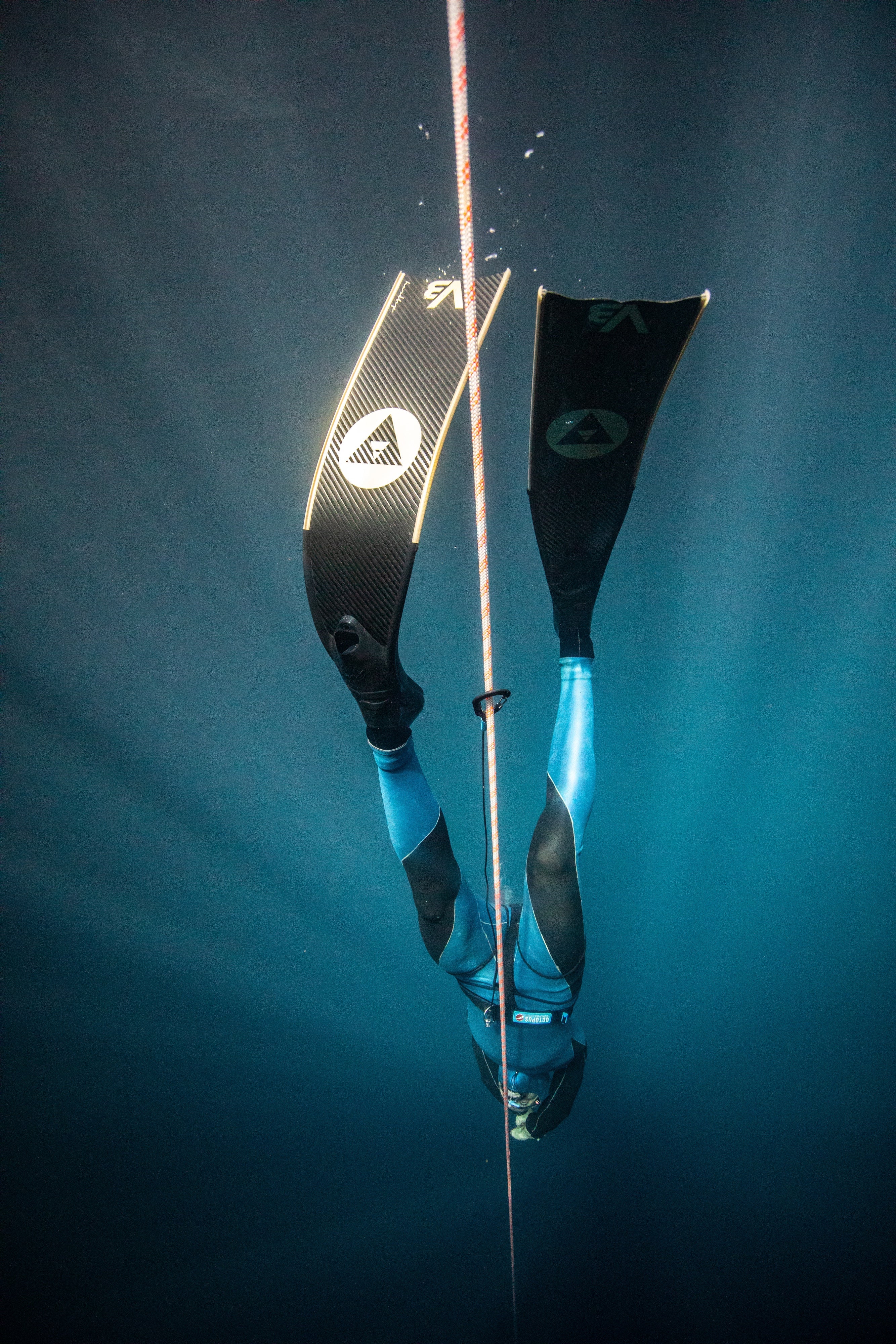 Freediver wearing a pair of Alchemy V3-30 fins in gold descending down the dive line.